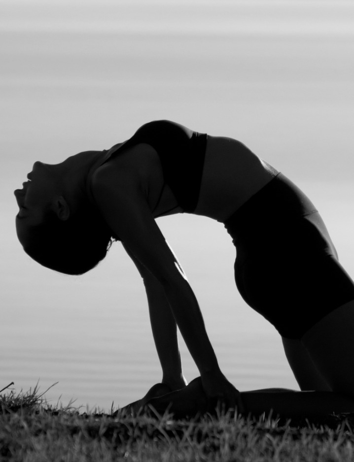 Yoga practitioner in a backbend silhouette by the water